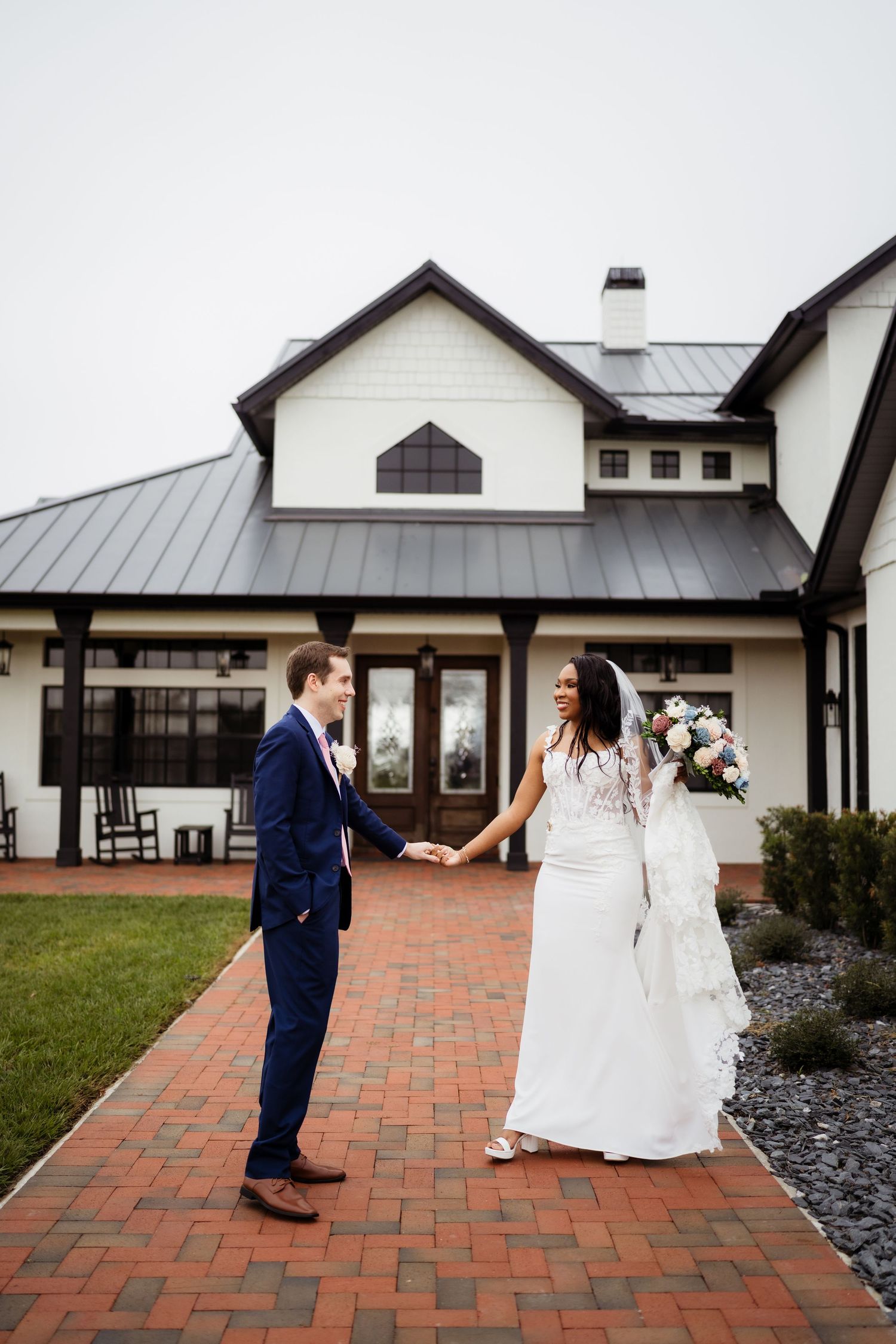 A bride and groom share a romantic first look moment on a brick patio outside a white farmhouse-style venue.