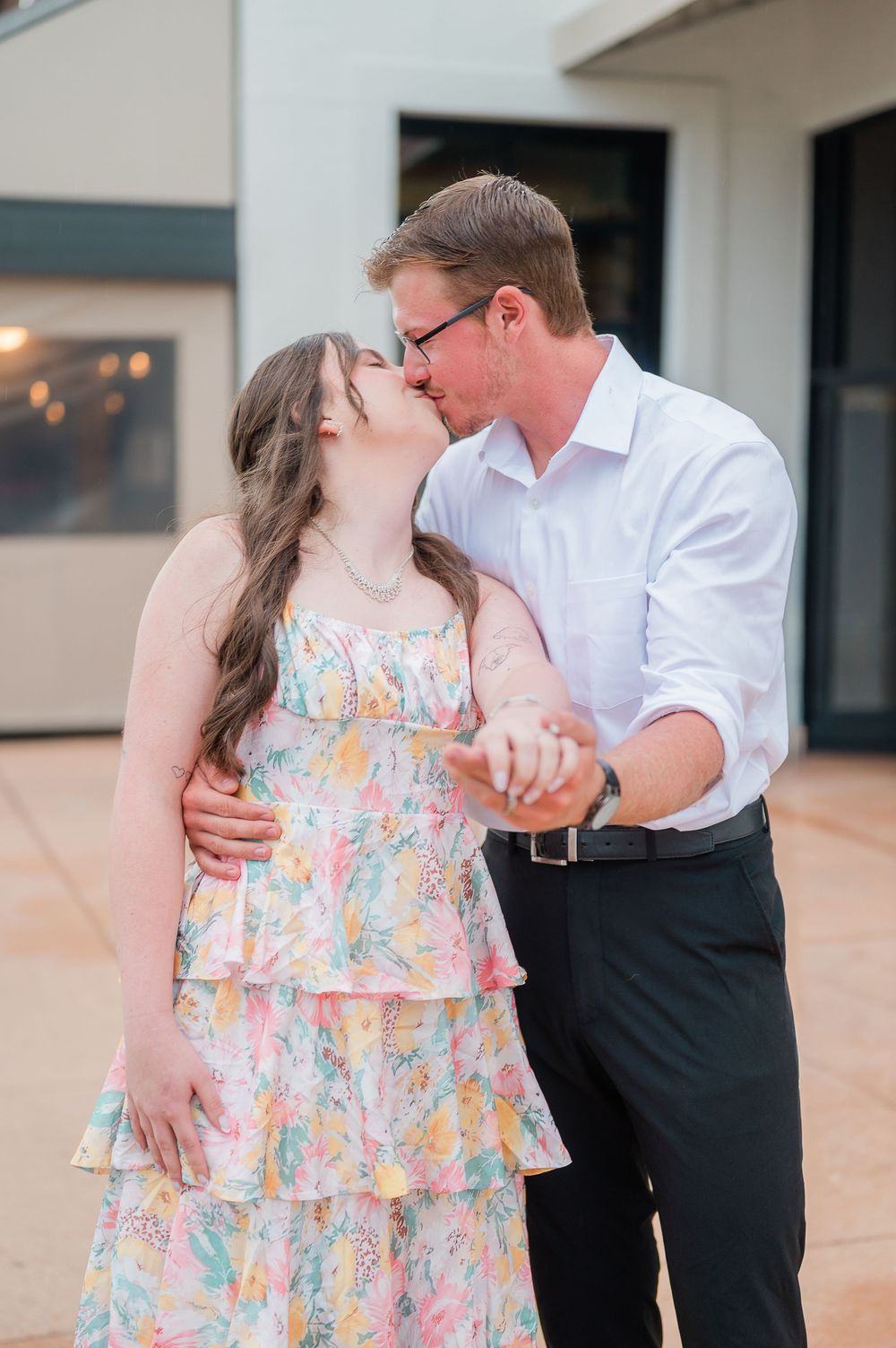 A couple shares a romantic moment outdoors, with the woman wearing a colorful floral sundress and the man in a white shirt.
