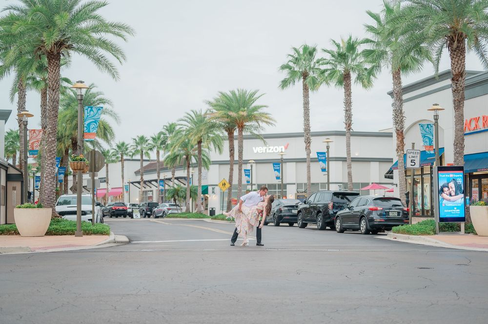 Palm trees line a commercial street with parked cars and businesses on a cloudy day.