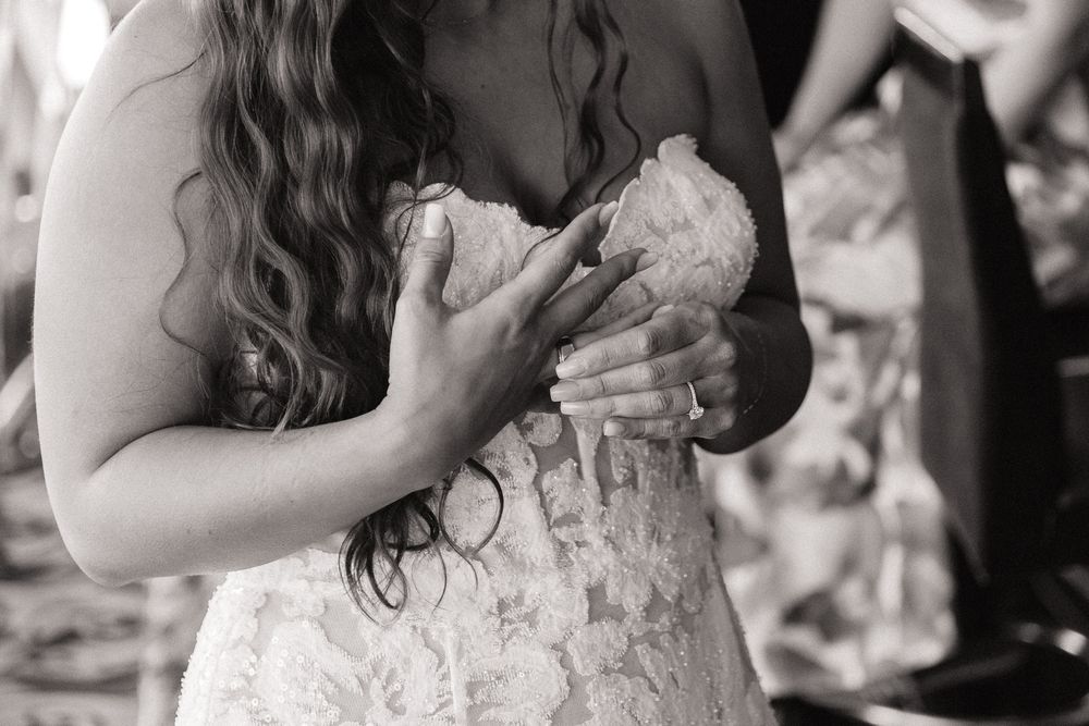 Bride in lace wedding gown clutches a bouquet close to her chest in black and white photo.