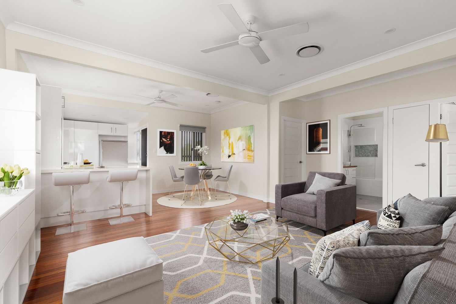 Bright living room with grey sofas, hardwood floors, ceiling fan, and open-plan connection to kitchen and dining area.