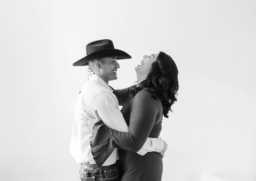 Black and white romantic portrait of a couple embracing, with one wearing a cowboy hat and western attire.