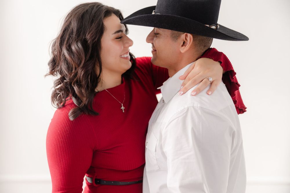 A couple in contrasting red and white outfits share an intimate moment against a white backdrop.