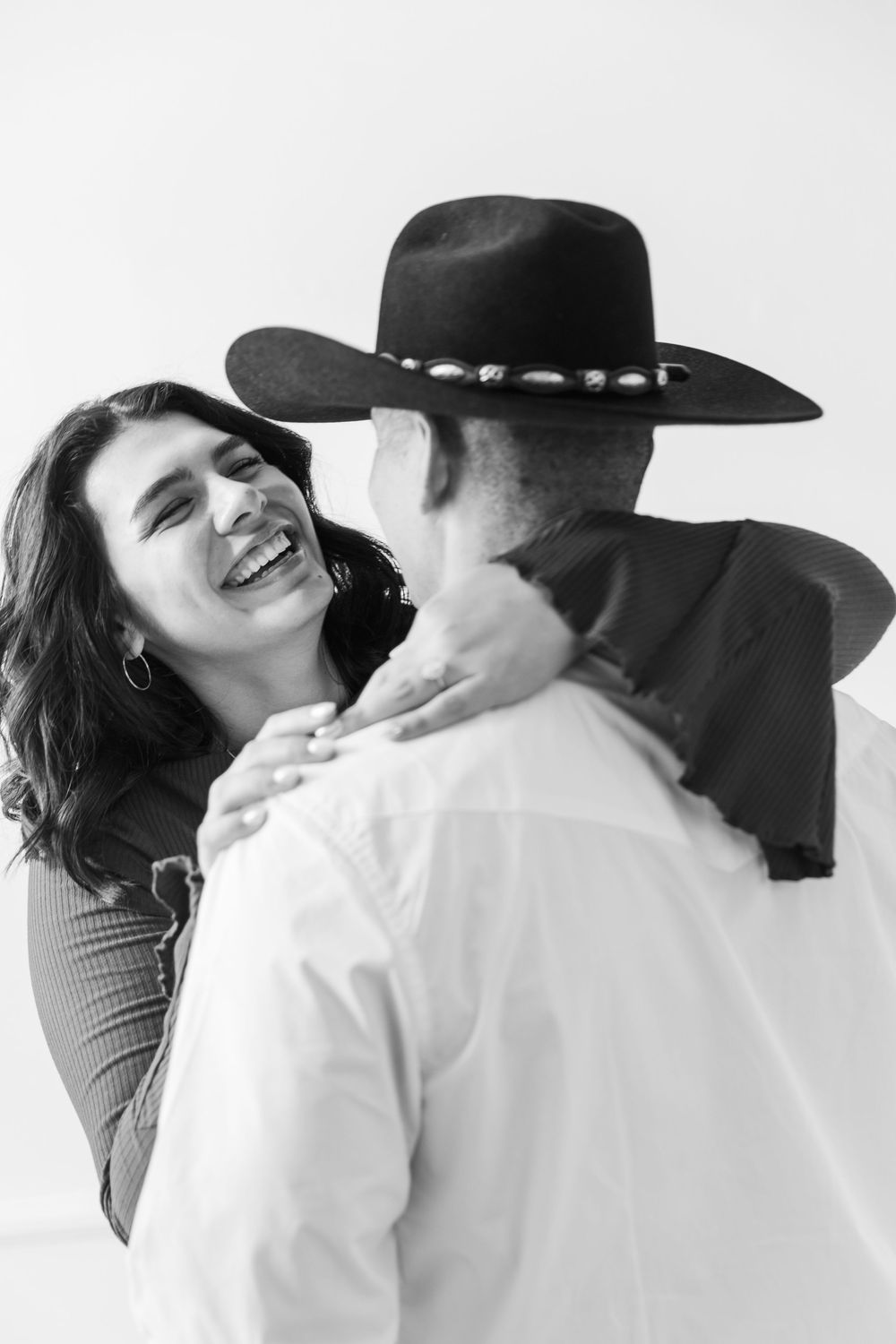 A couple shares a joyful candid moment together, with one wearing a black cowboy hat in black and white photography.