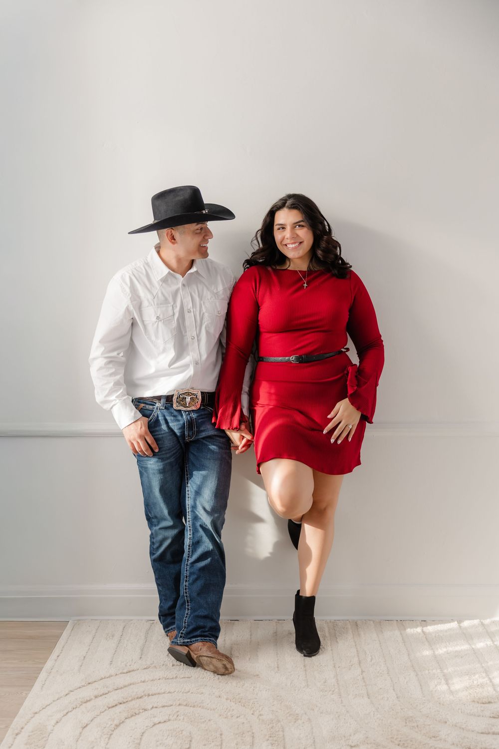 A couple in a white and red outfit sits together on a white bench in a minimalist studio setting.