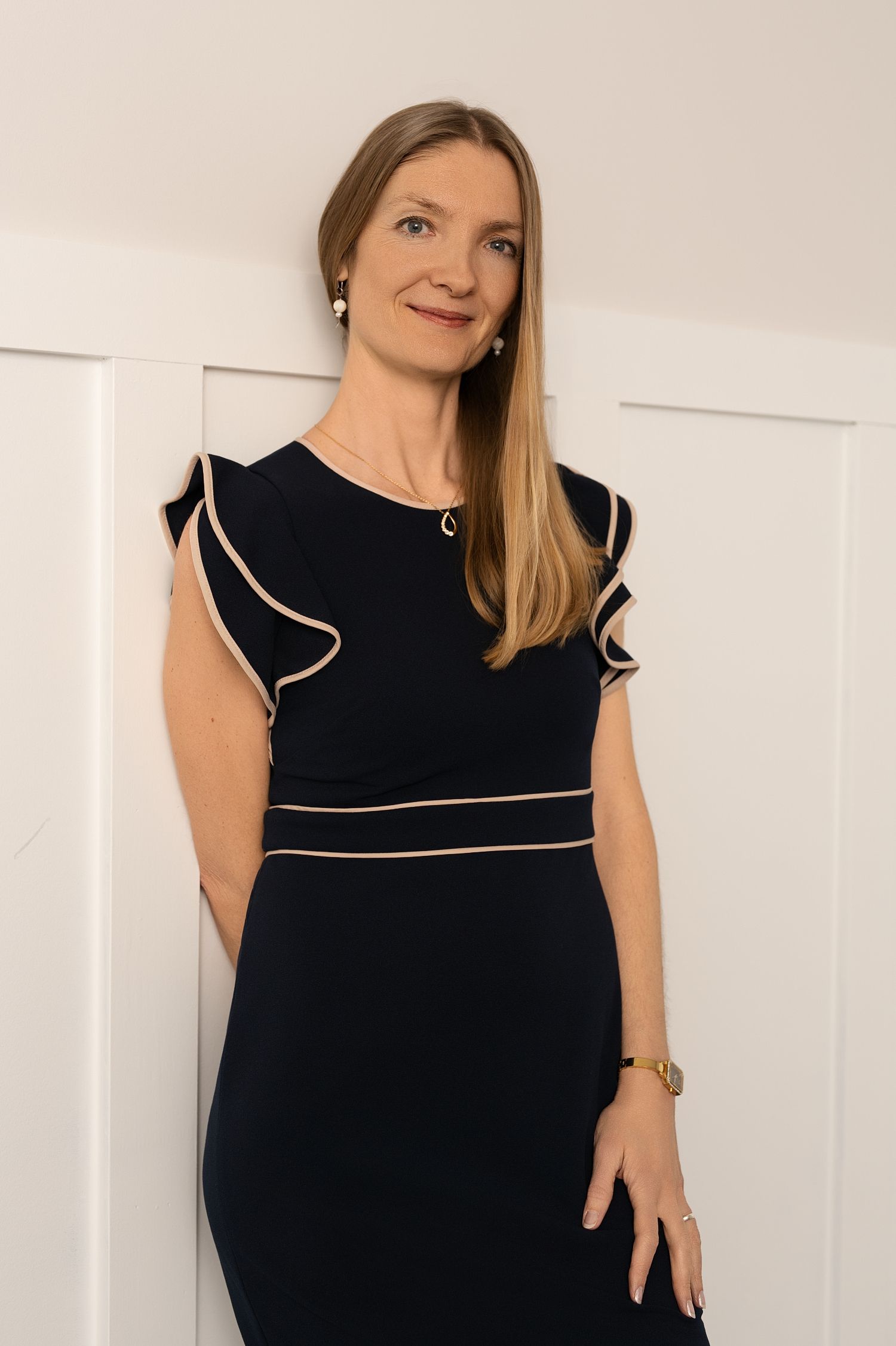 Woman wearing a black dress with white piping trim poses in four different angles against a white wall.
