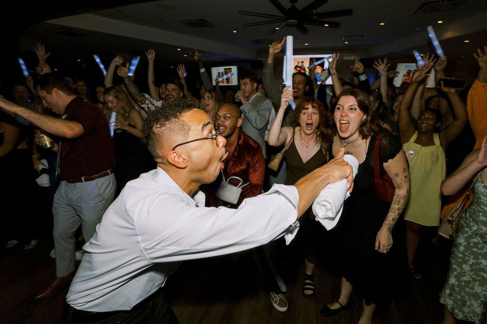 Man excitedly pointing and dancing with guests during a fun reception with light sticks.