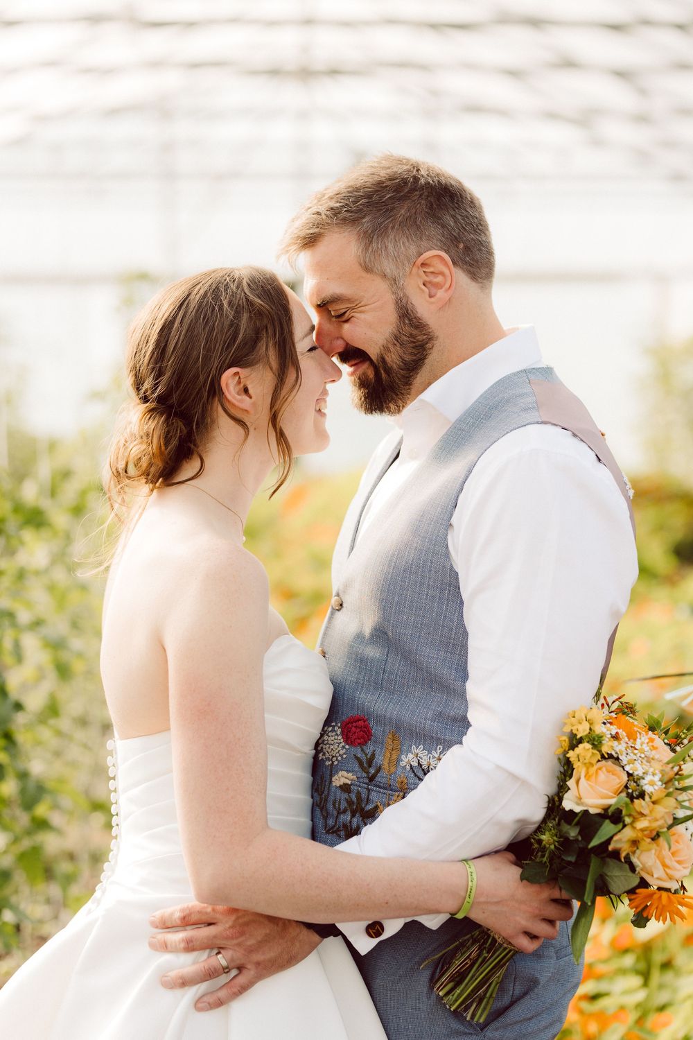 Romantic wedding moment with couple touching foreheads as bride holds colorful autumn bouquet in outdoor setting.