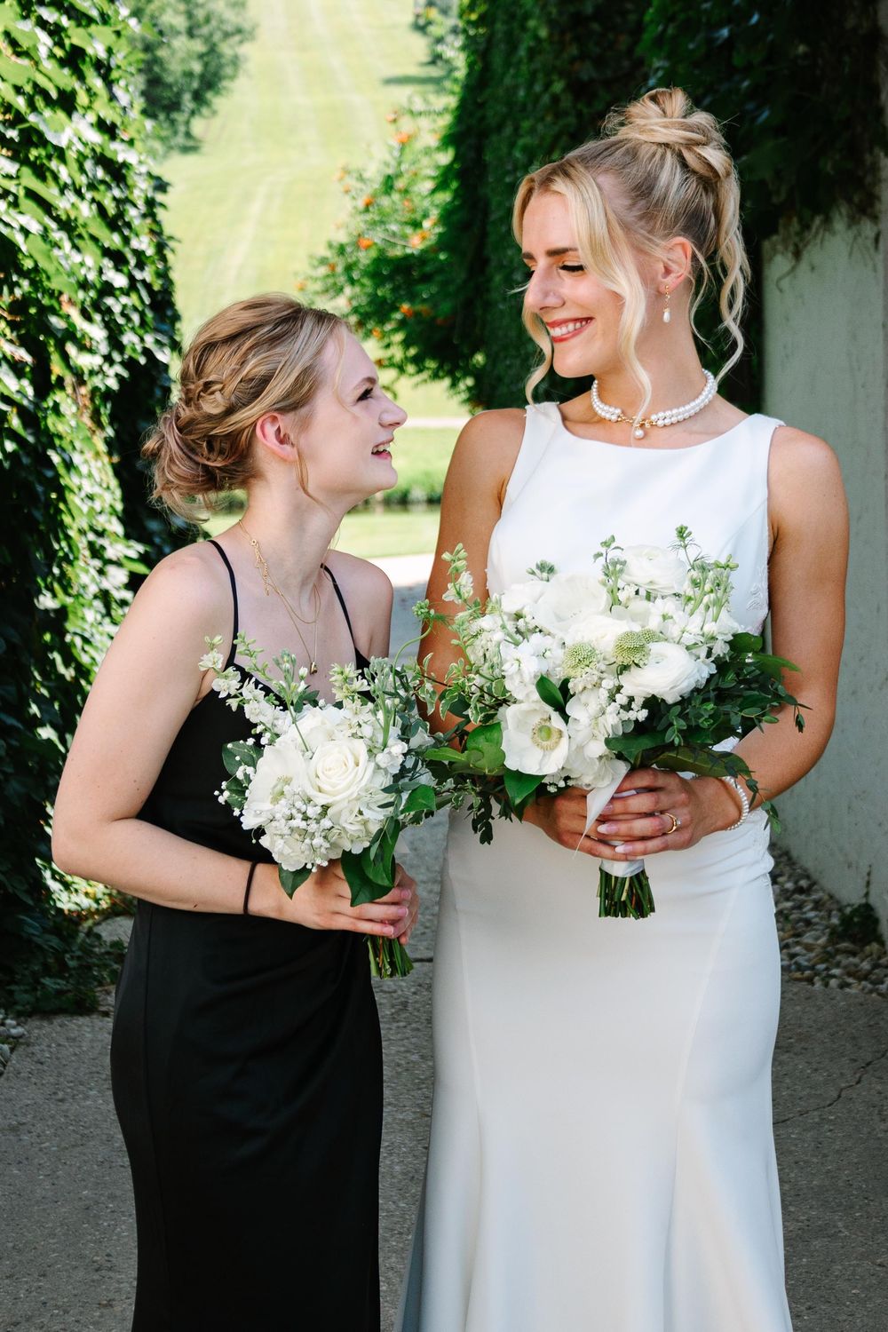 Two people in contrasting black and white dresses hold white floral bouquets while sharing a tender moment outdoors.