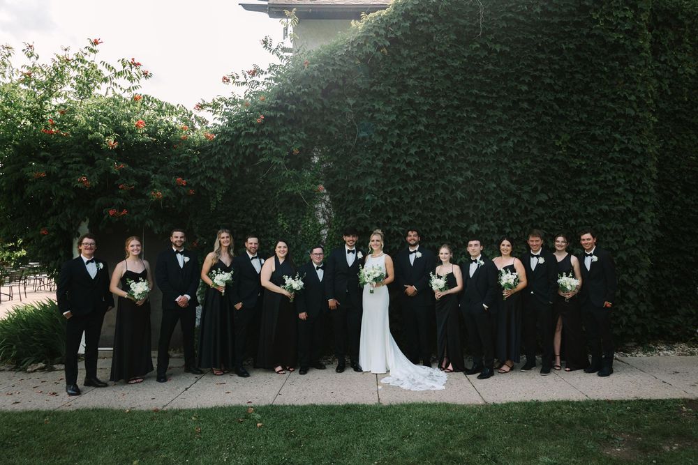Wedding party poses in a line outdoors at sunset against a backdrop of lush green trees.