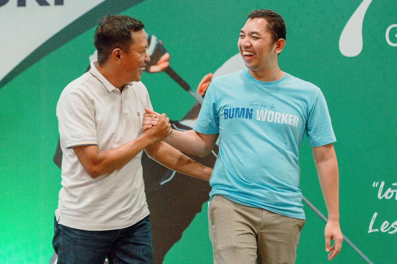 Two men in casual attire share an animated conversation against a green backdrop.