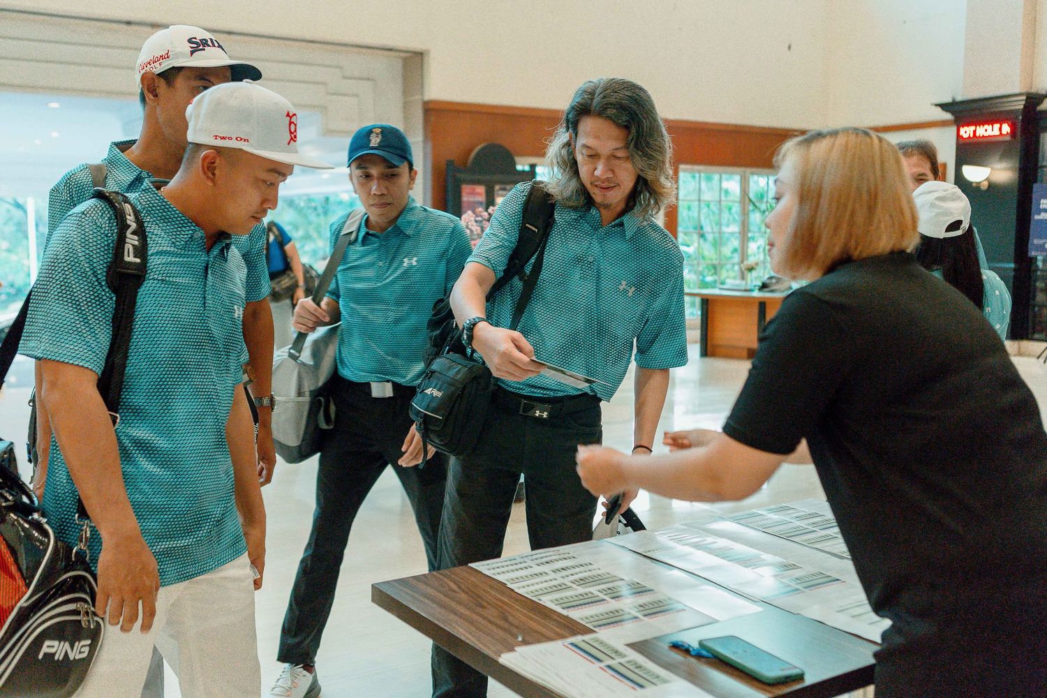 A group of people wearing teal colored uniforms gather around tables in an indoor space.