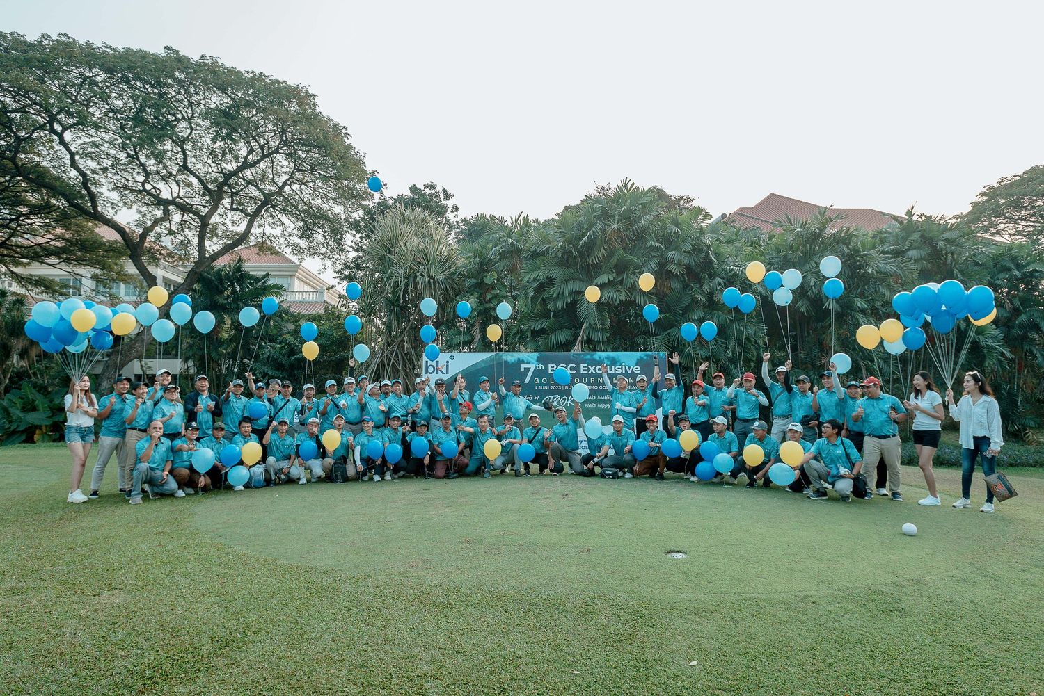Large group wearing matching blue shirts gathered outdoors for a community event with colorful balloons in the background.