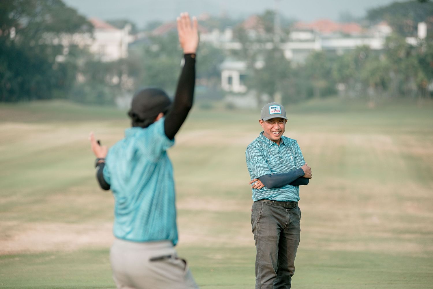 Two golfers celebrating on a misty golf course with houses in the background.