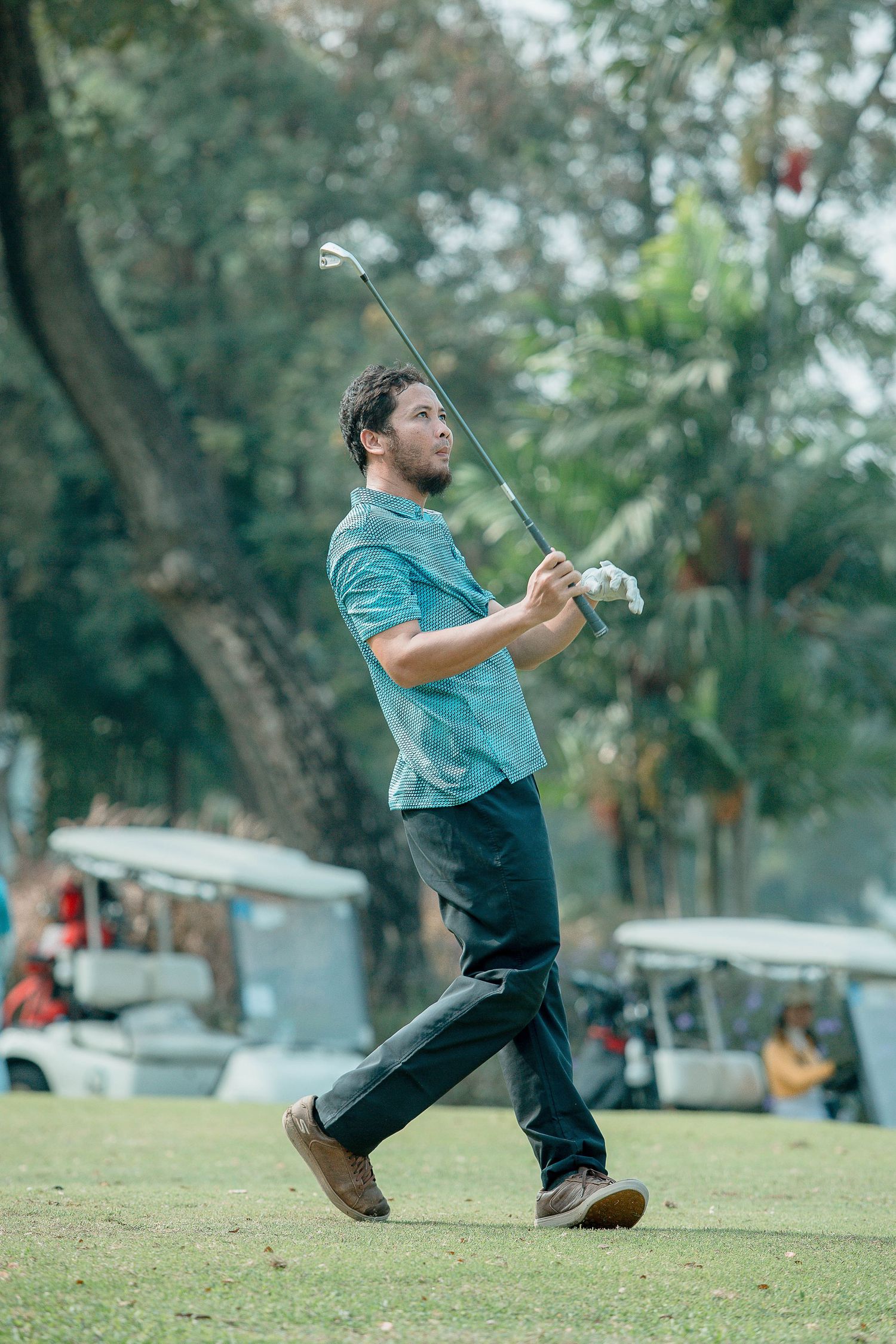 A golfer in a teal shirt demonstrates a complete golf swing sequence on a grassy course.