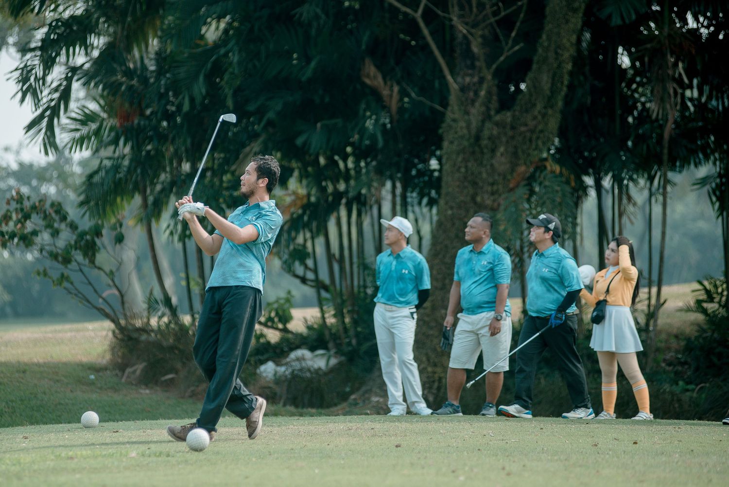 Group of people practicing golf on a lush green course surrounded by evergreen trees.