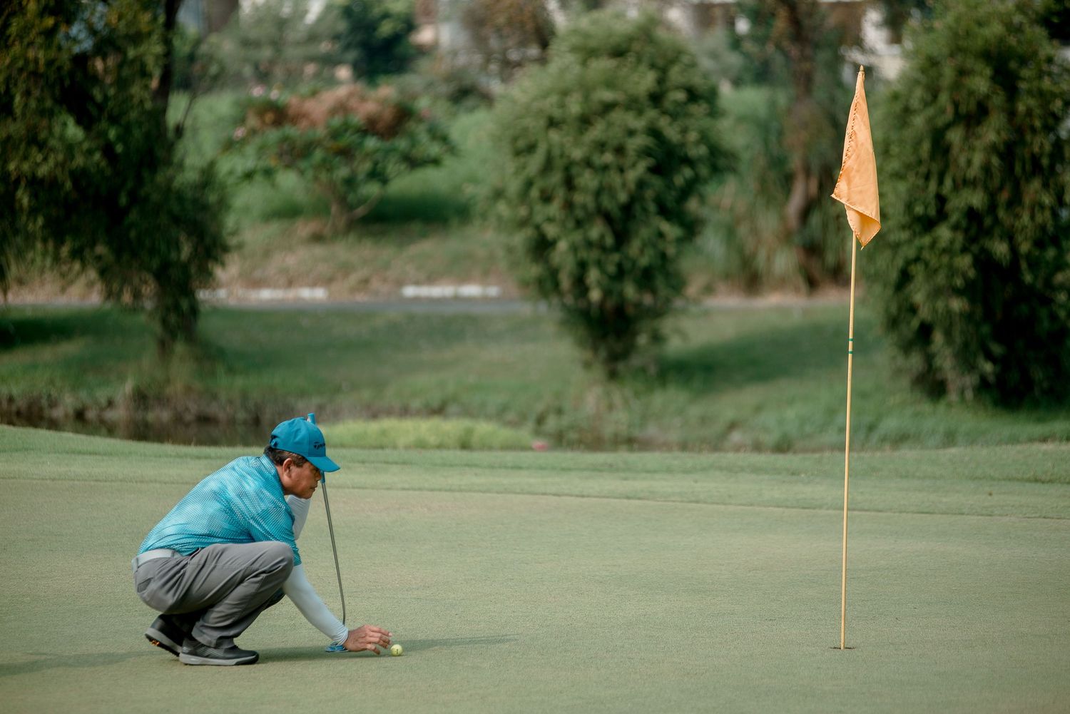 Golfers lined up on a putting green practicing their shots near a yellow flag.