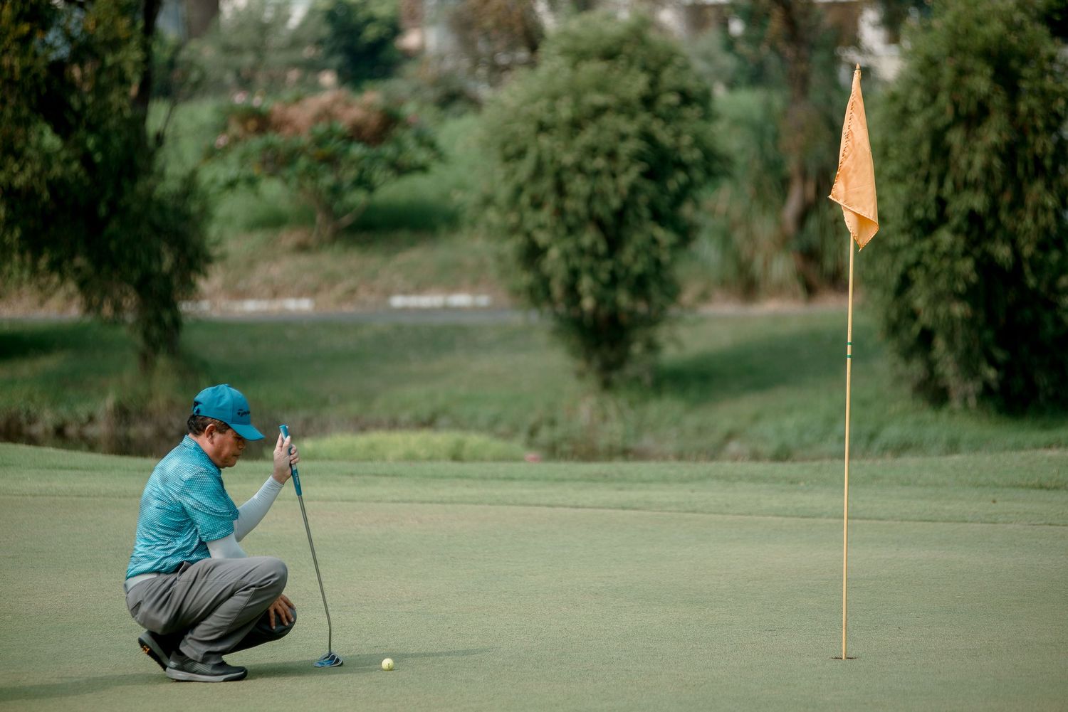 Golfer crouching to analyze the putting green with yellow flag marker visible.