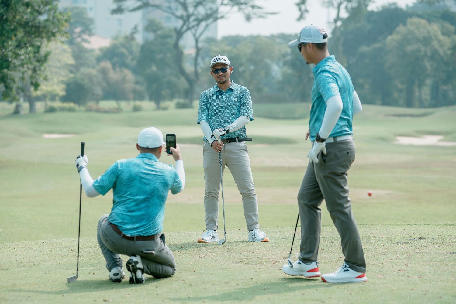 Golfers in turquoise shirts marking positions and placing balls on a sunny golf course.