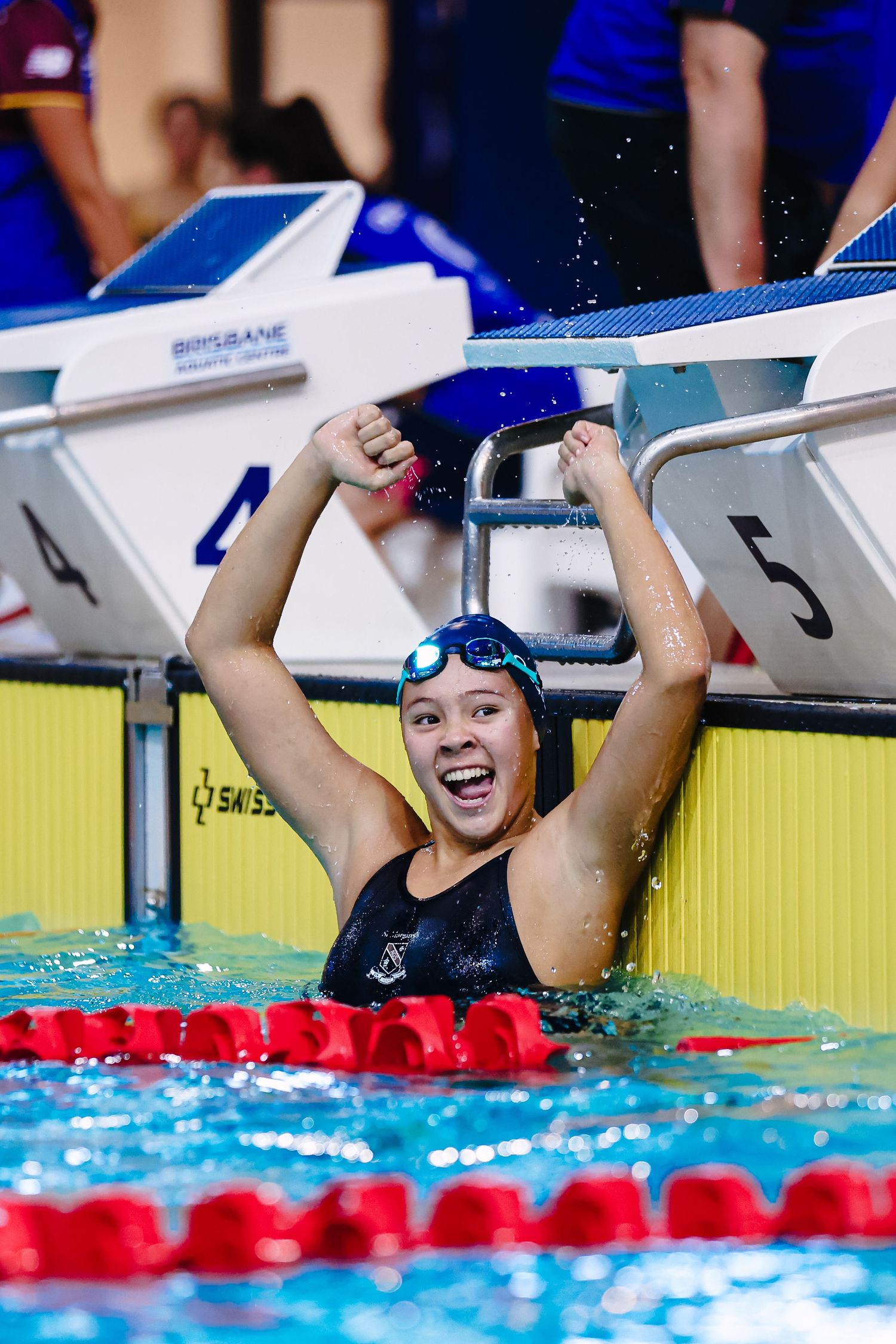 Swimmer celebrates victory in swimming competition with arms raised in joy while still in the pool lane.