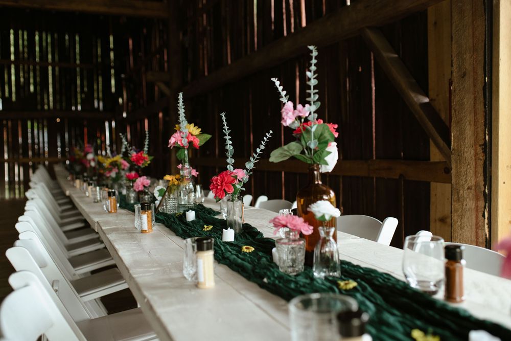 Long rustic wooden dining tables decorated with elegant floral arrangements and candles for an indoor wedding reception.