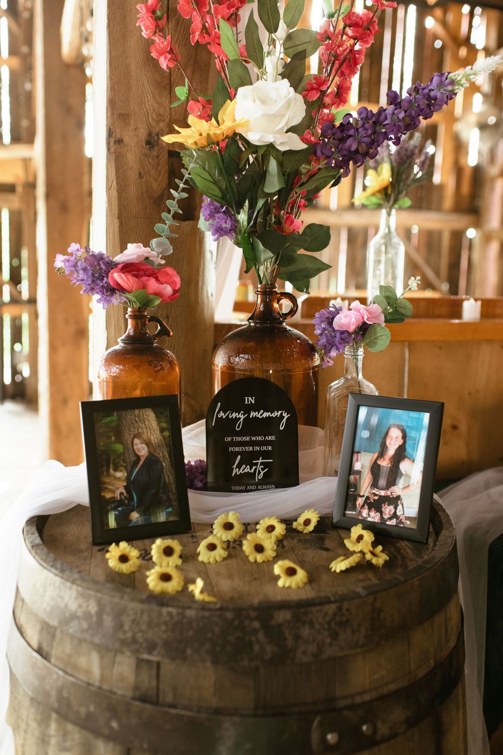 Wine barrel decorated with flowers and picture frames creates a rustic display at a barn venue.