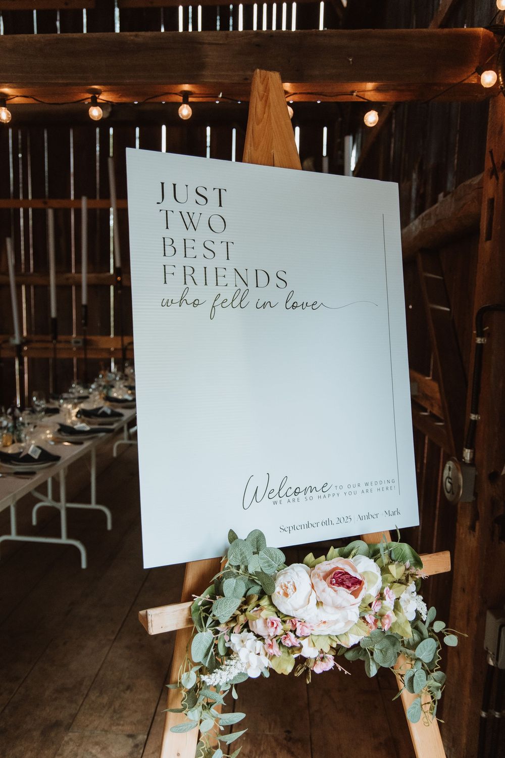 Wedding reception signs decorated with floral arrangements and eucalyptus displayed in rustic barn venue setting.