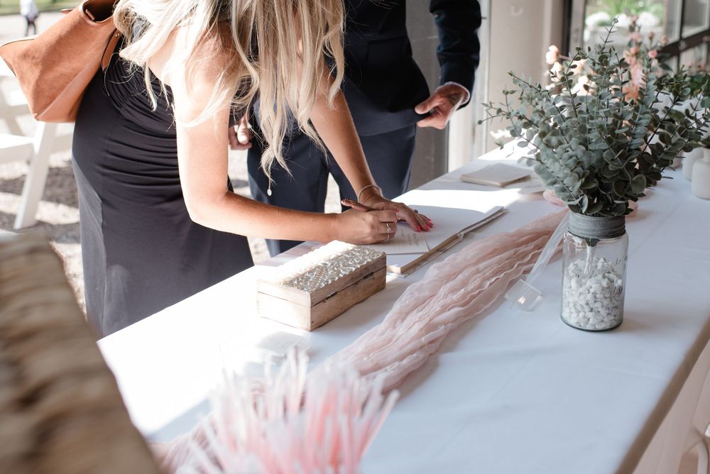 People signing a wedding guest book at a white-clothed table with decorative elements.