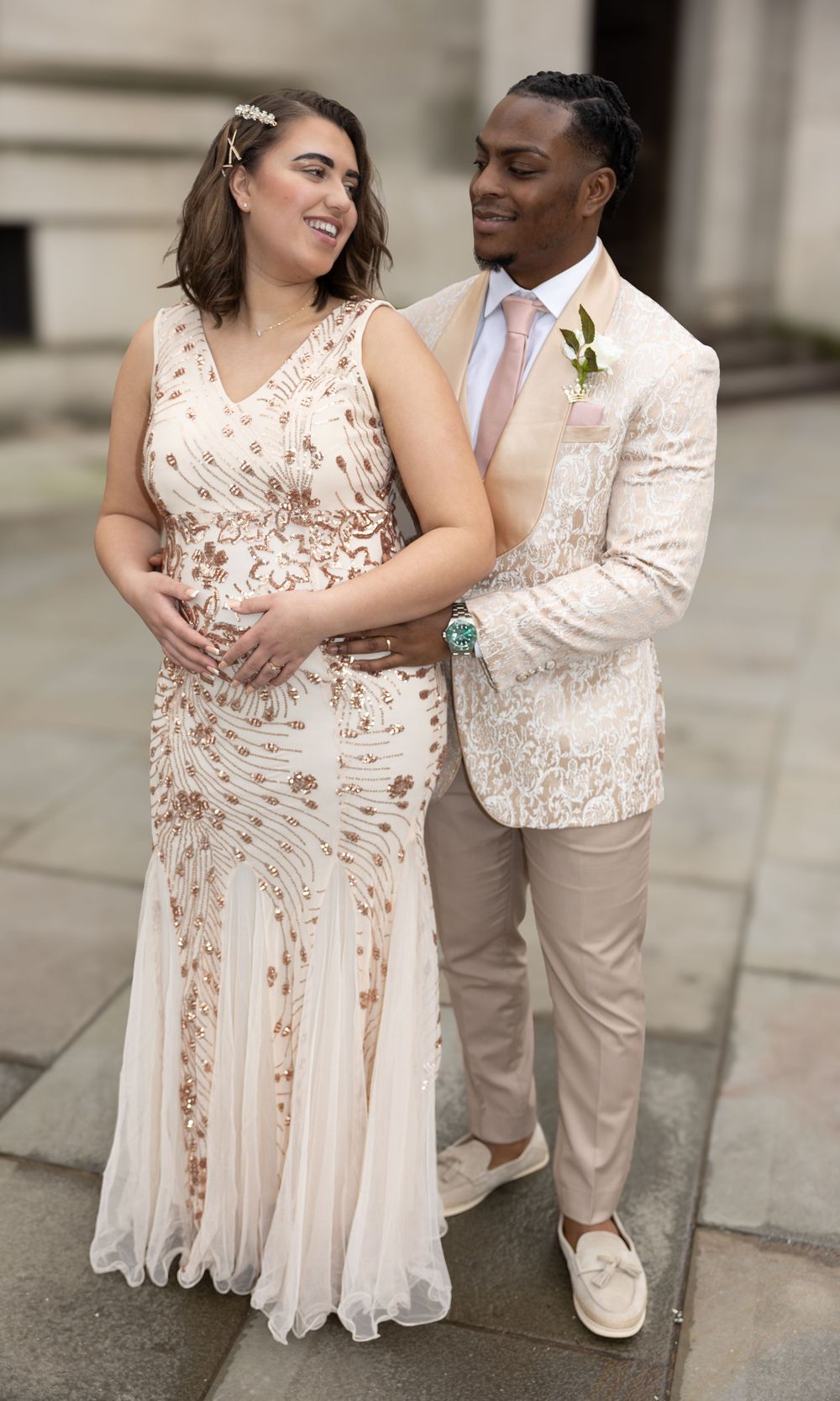 A couple poses together at a formal event wearing matching cream and blush tones with elegant floral details.