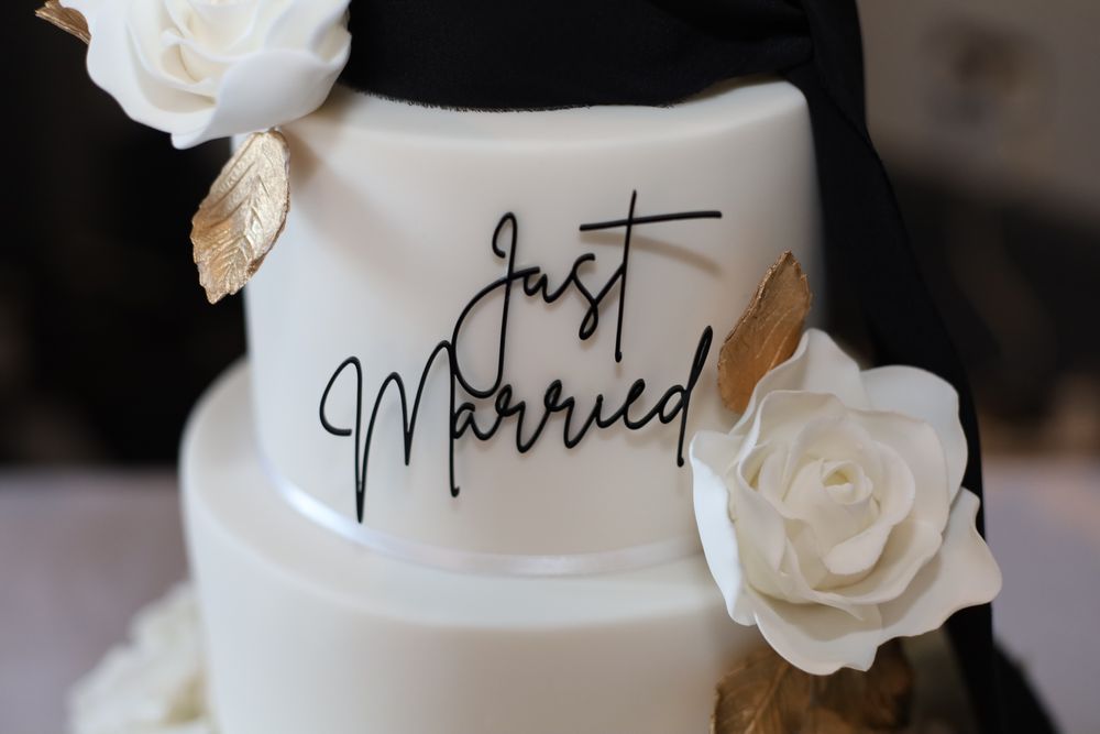 White wedding cake decorated with 'Just Married' script and delicate white roses against a dark background.