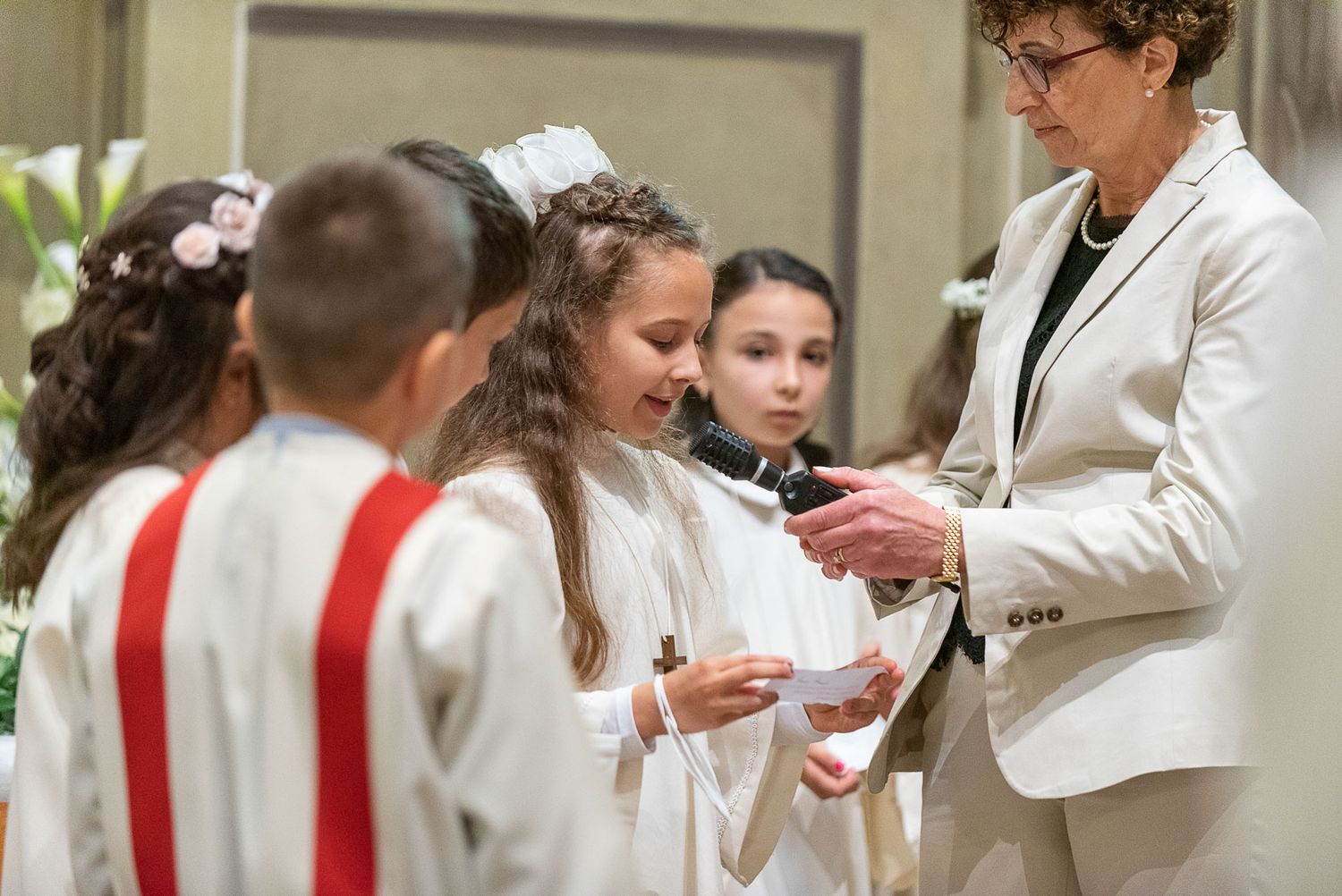 Young altar servers in white vestments receiving instruction during a church ceremony.