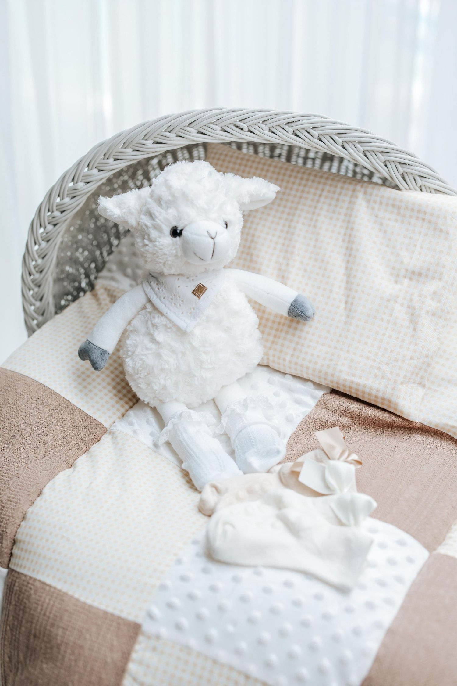 White plush lamb toy sitting on a cozy chair with textured pillows and blankets in soft neutral tones.