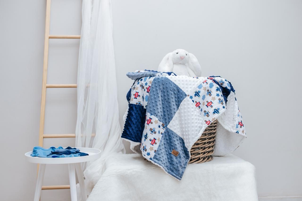 Baby blankets in blue and white patterns with stars displayed on white furniture against a light wall.