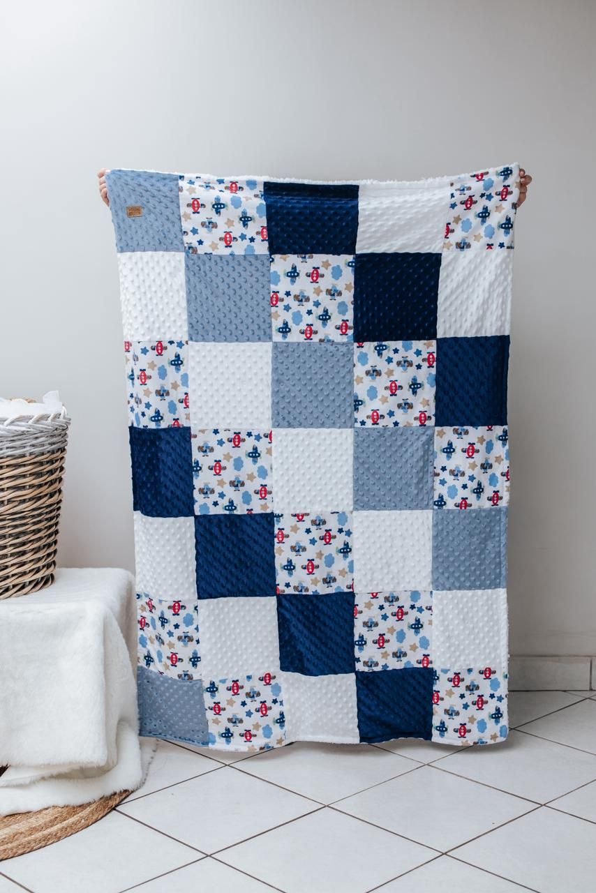 Patchwork quilt with blue, white and floral squares displayed against a white wall near a woven basket.