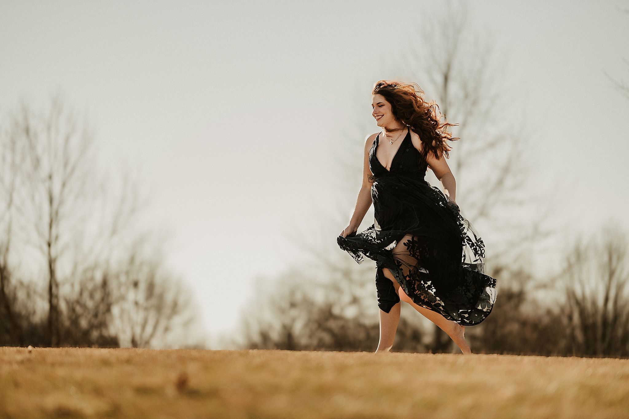 A person in a black dress spins gracefully in a field at sunset with hair flowing in the wind.