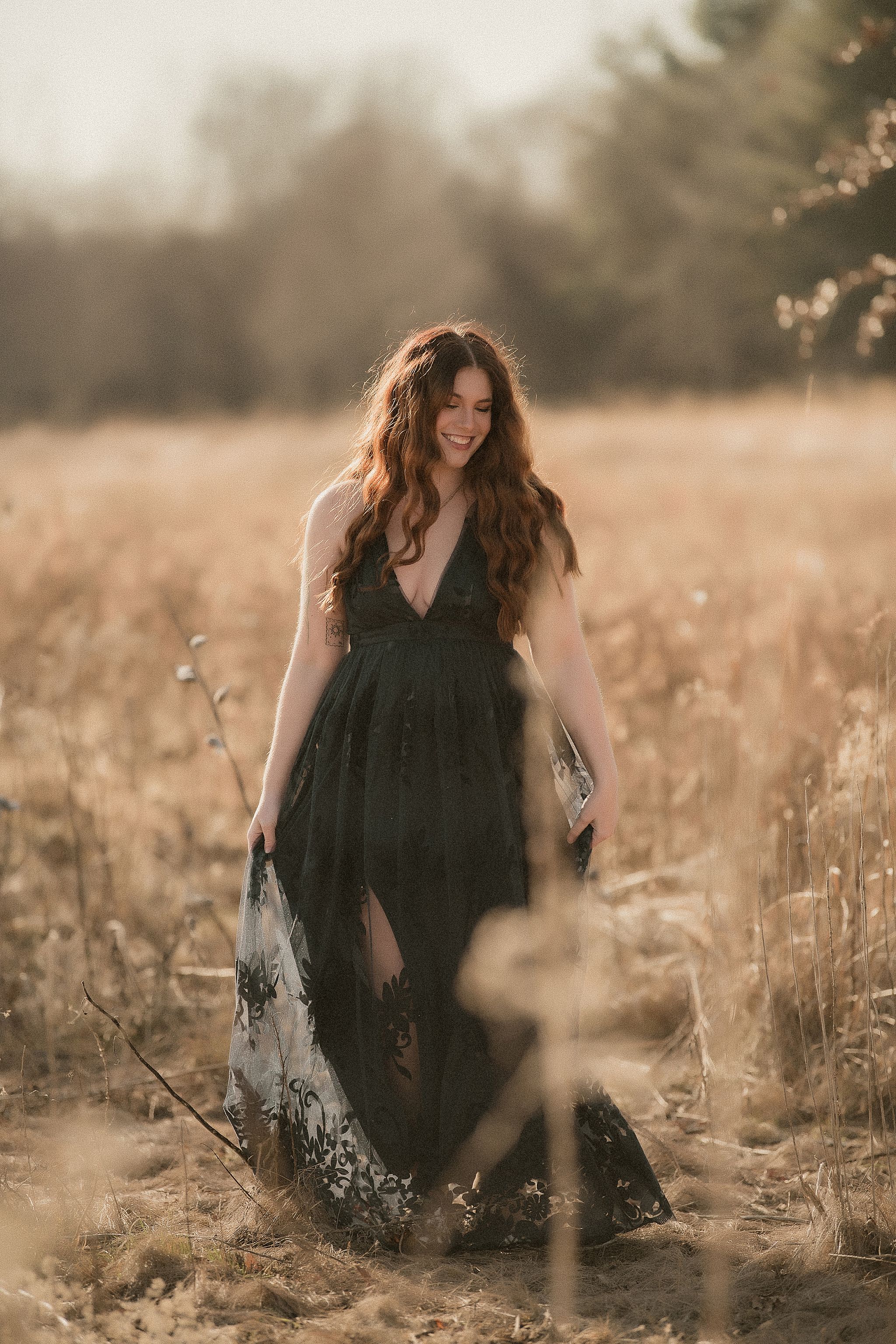 A person in a black dress sits in a golden field at sunset creating a dreamy, ethereal atmosphere.