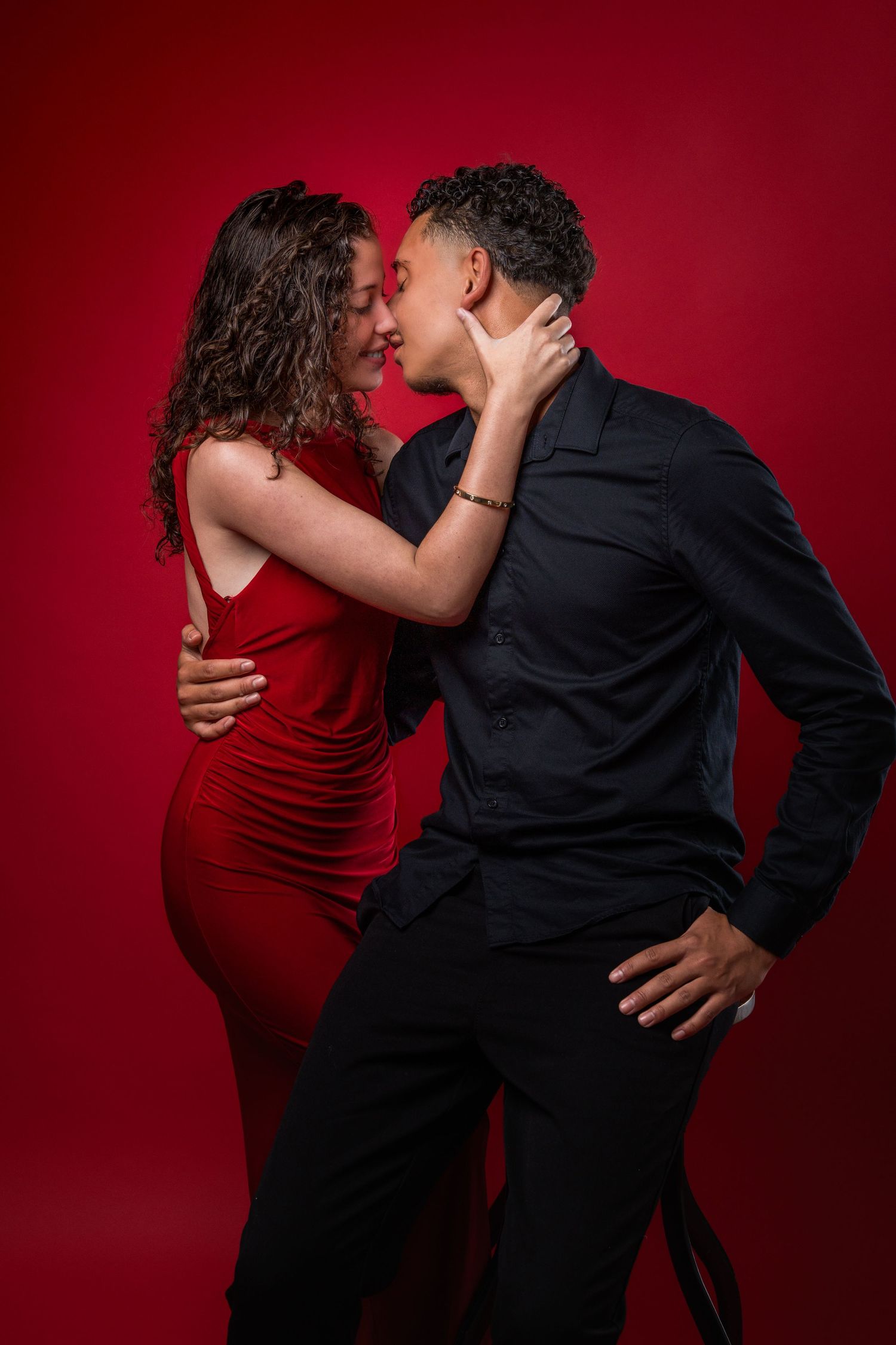 Couple in contrasting black and red outfits share intimate moment against crimson background.