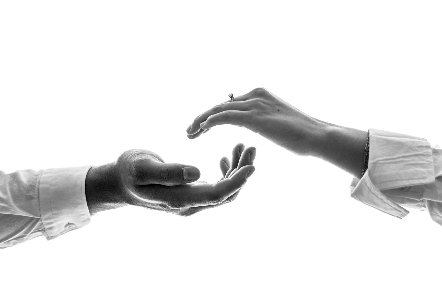 Black and white artistic photograph of two reaching hands in white sleeves against a white background.