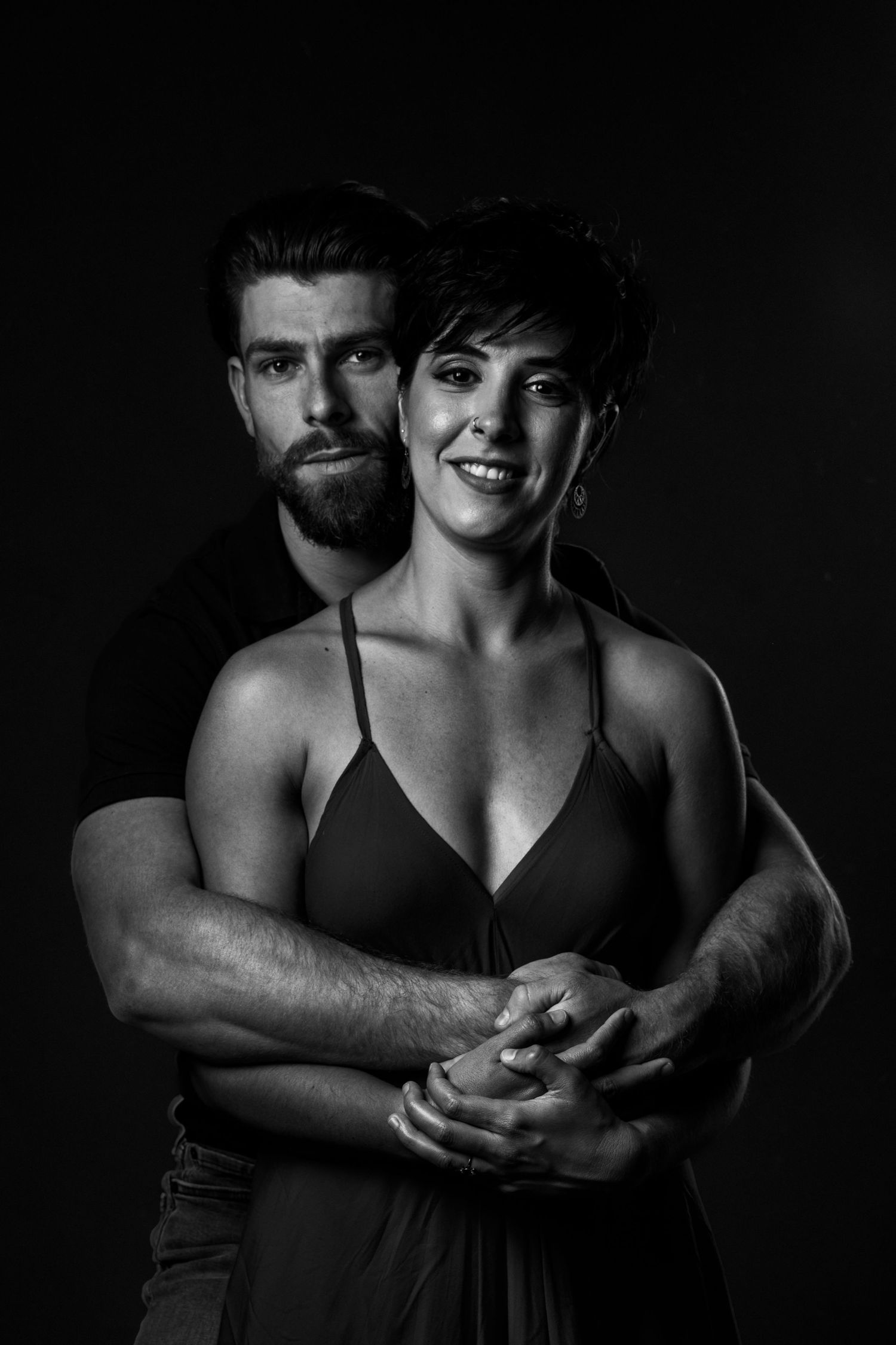 A black and white portrait of a couple embracing in dramatic lighting against a dark background.