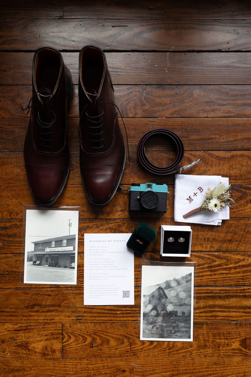 Groom wedding flat lay with brown leather boots, camera, rings, and accessories on wood floor.