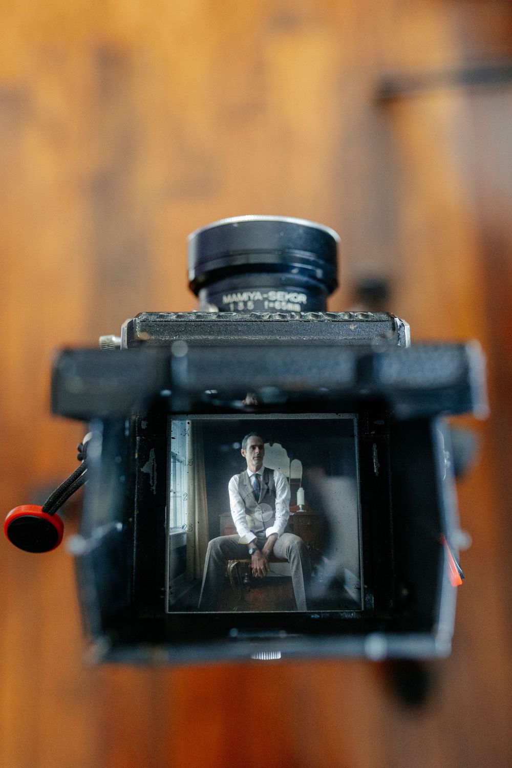 Groom reflected in vintage medium format camera viewfinder while getting ready for wedding.