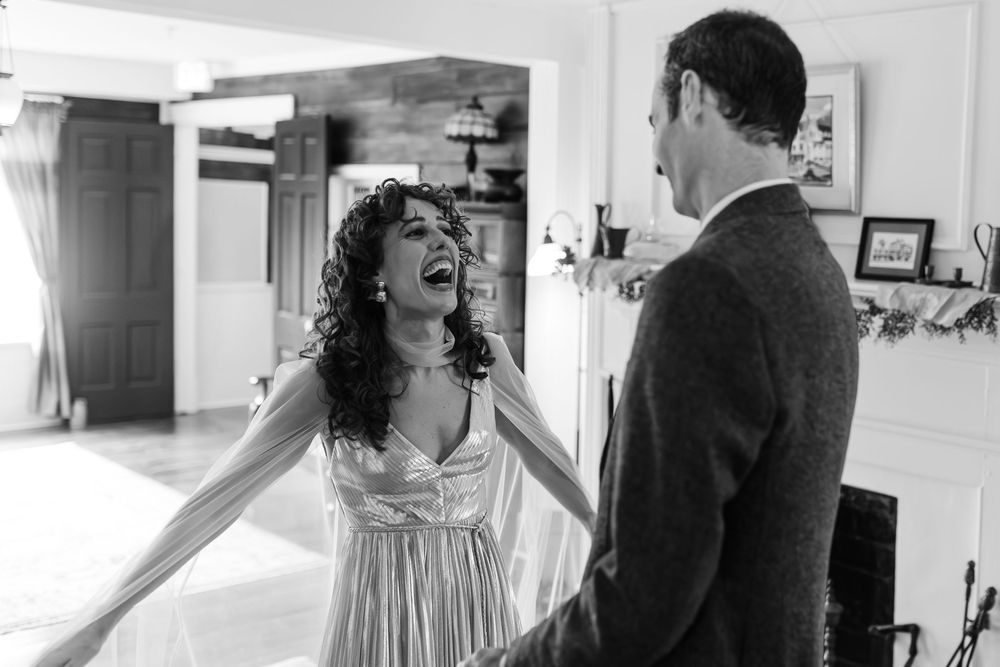 Bride laughs joyfully during emotional first look with groom in black and white wedding portrait indoors.