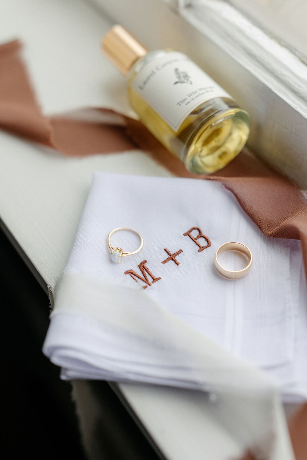 Wedding details flat lay with gold rings on monogrammed handkerchief and perfume bottle.