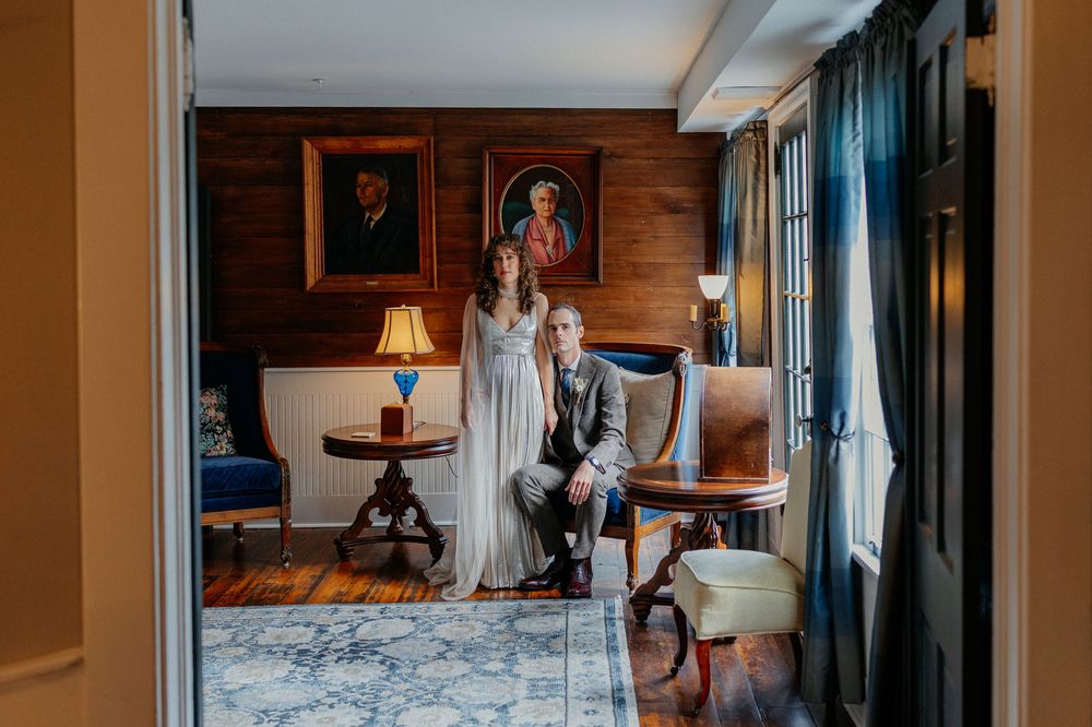 Bride and groom pose together in elegant wood-paneled room with portrait paintings and vintage decor.