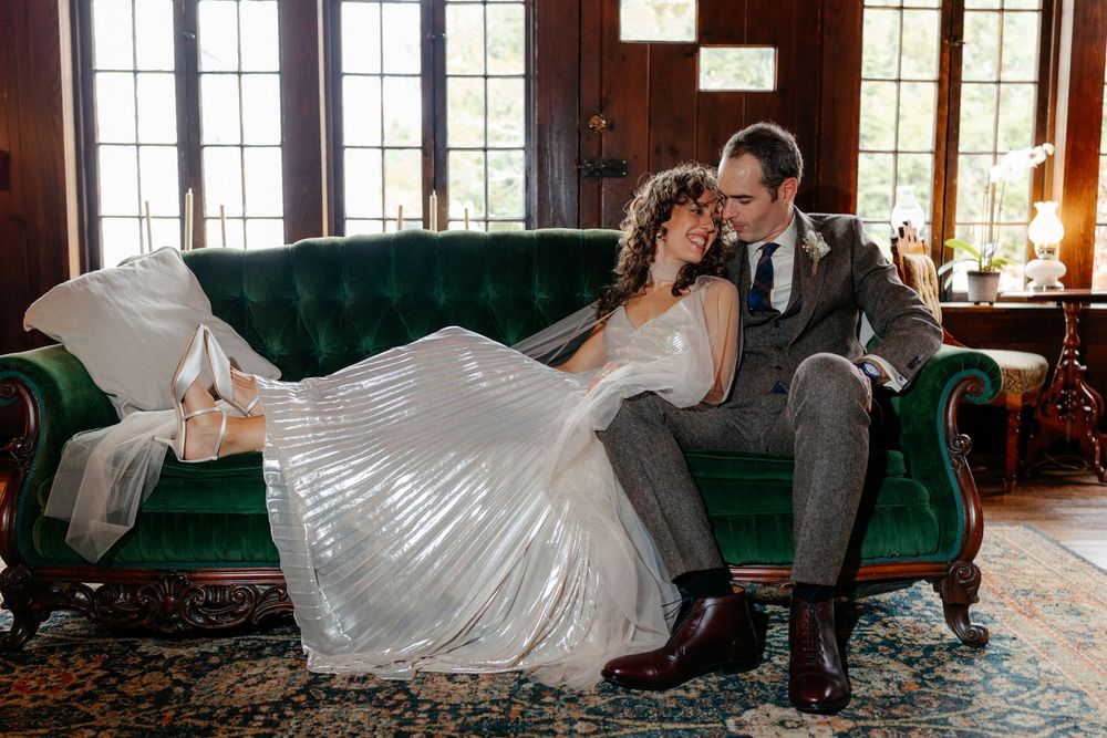 Bride and groom share intimate moment on green velvet tufted sofa in vintage-styled wedding portrait.