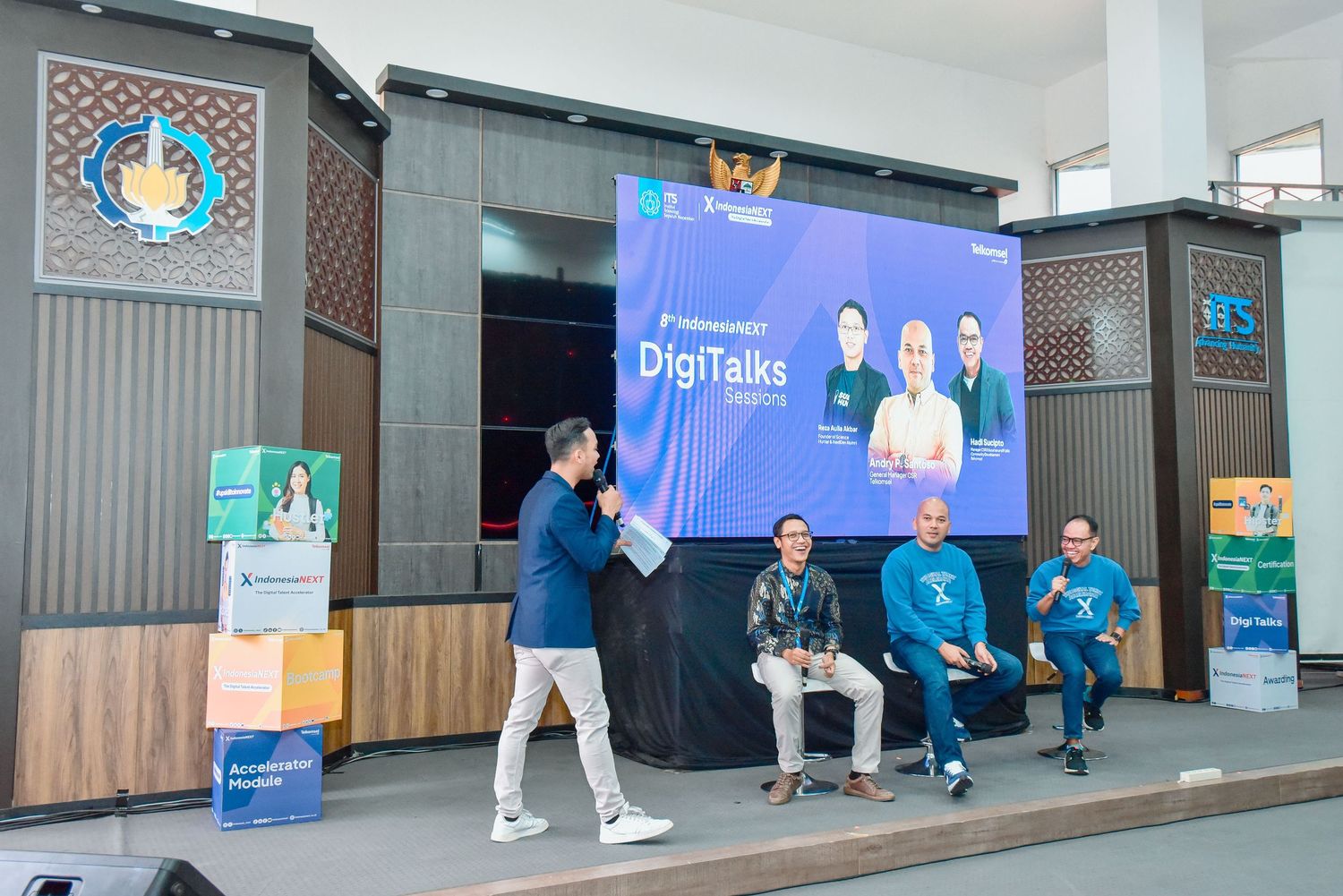 A panoramic view of a conference hall with blue displays and presentation screens along the walls.