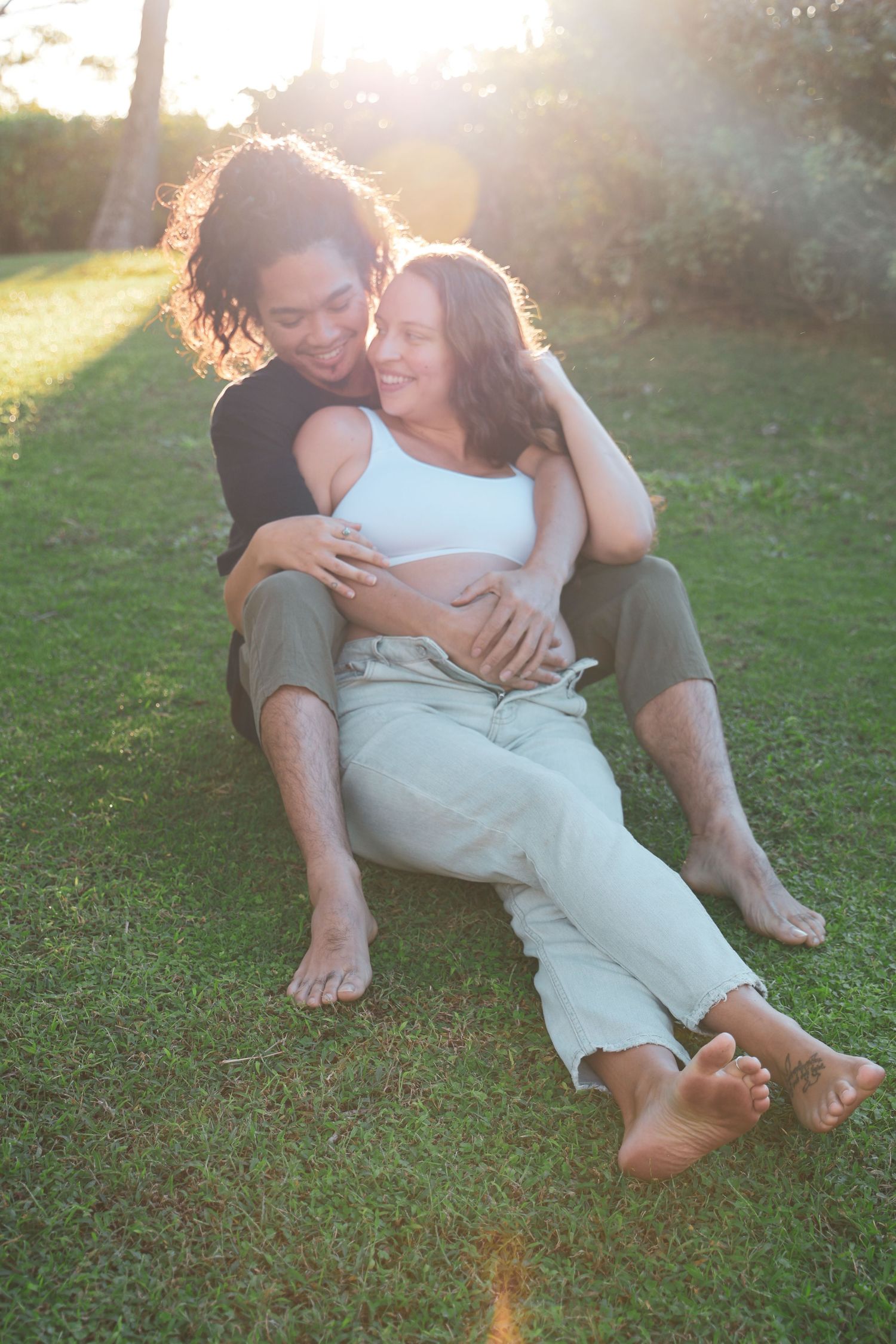 A couple sits together on grass during golden hour, sharing an intimate embrace in a series of romantic poses.
