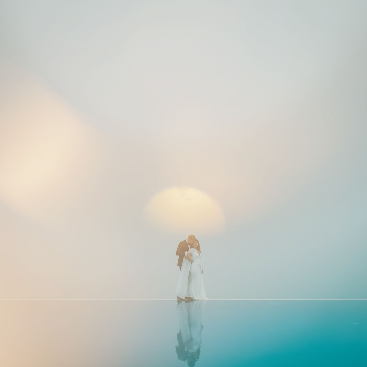 A dreamy minimalist seascape shows a lone figure reflected in calm turquoise waters under a soft pastel sky.