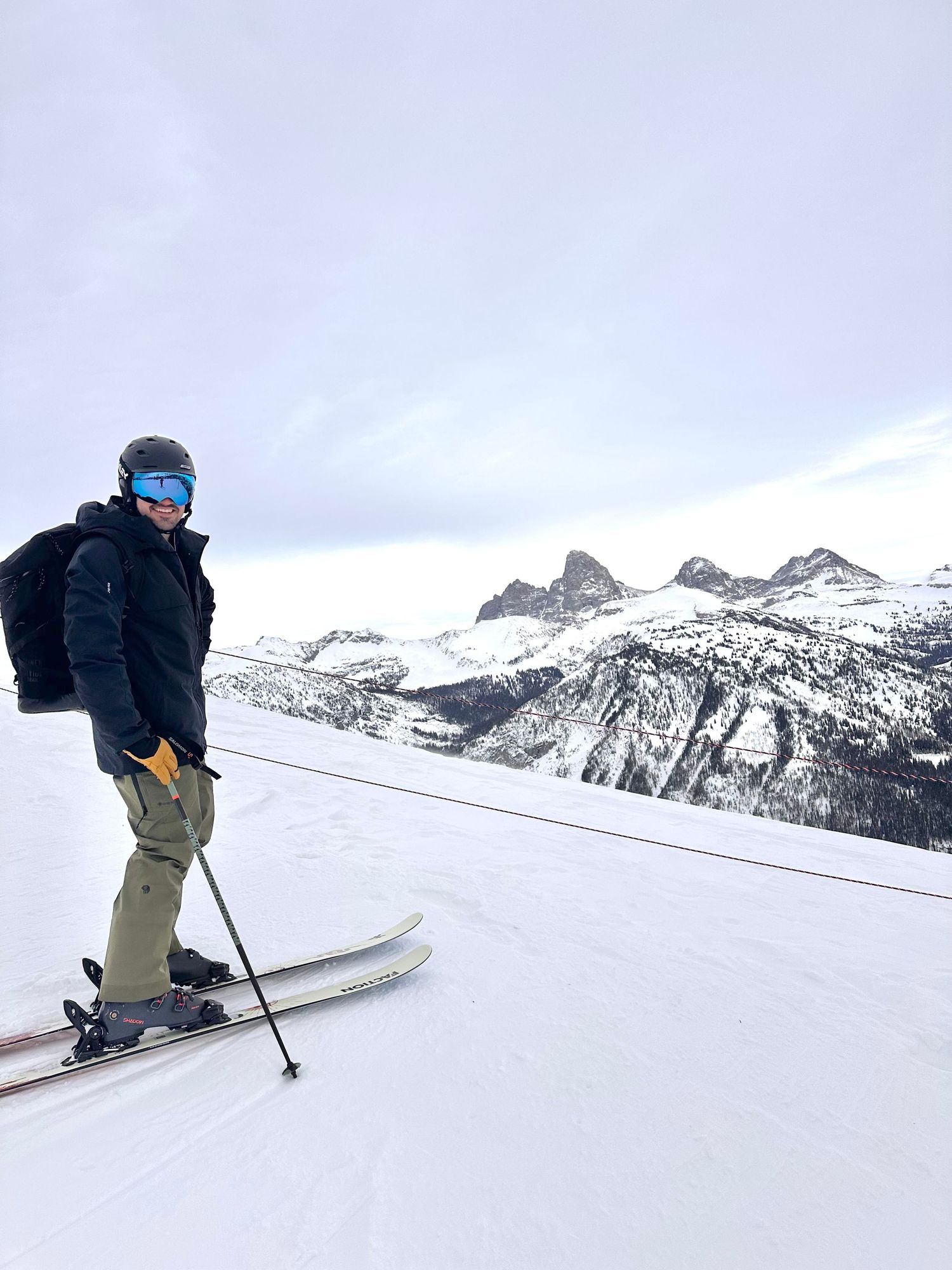 Skier posing on snowy mountain slope with dramatic rocky peaks visible in the background.