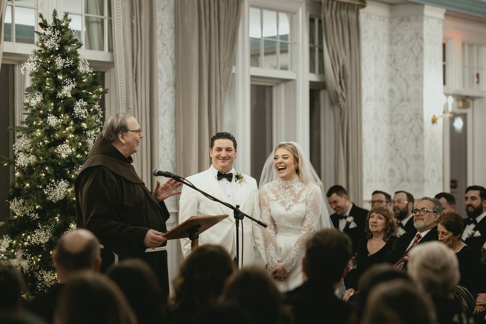 Wedding guests mingle and socialize in an elegant reception hall with tall windows and luxurious curtains.